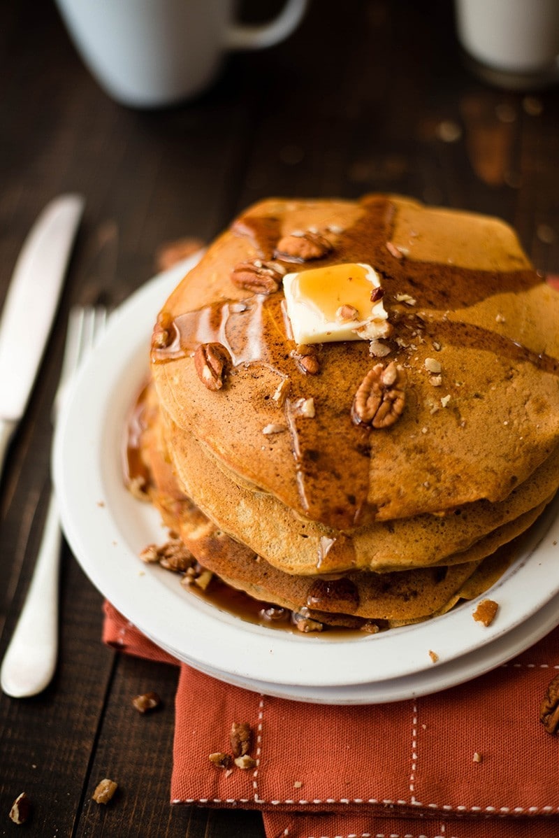 Close up of a stack of Healthy Pumpkin Pancakes, with butter and pure maple syrup, served on a white plate
