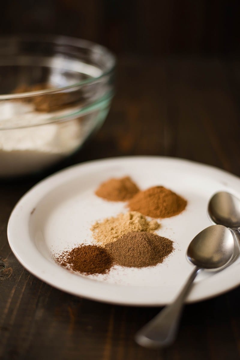 Close up view of spices for Healthy Pumpkin Pancakes on a white plate, along with two spoons