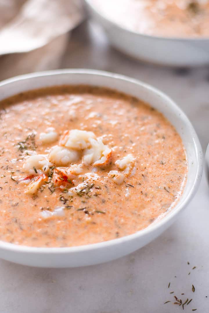 Side view of a bowl of easy lobster bisque which is garnished with lobster and thyme.