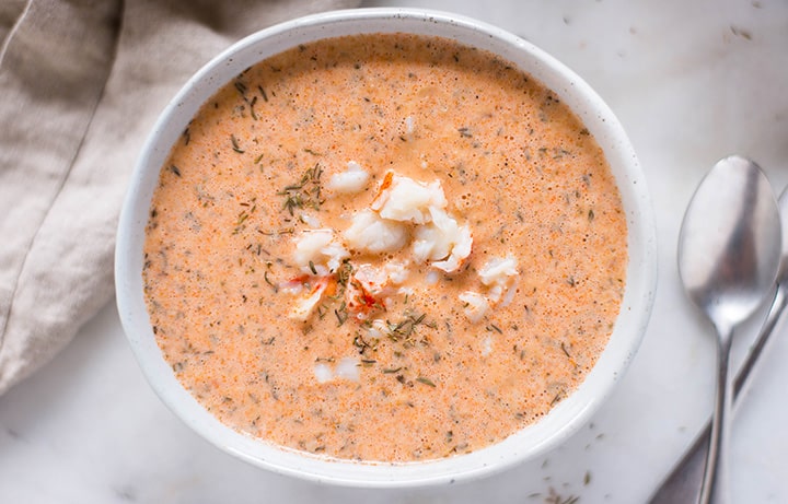 Horizontal view of a bowl of lobster bisque which is topped with a pile of cooked lobster chunks and thyme.