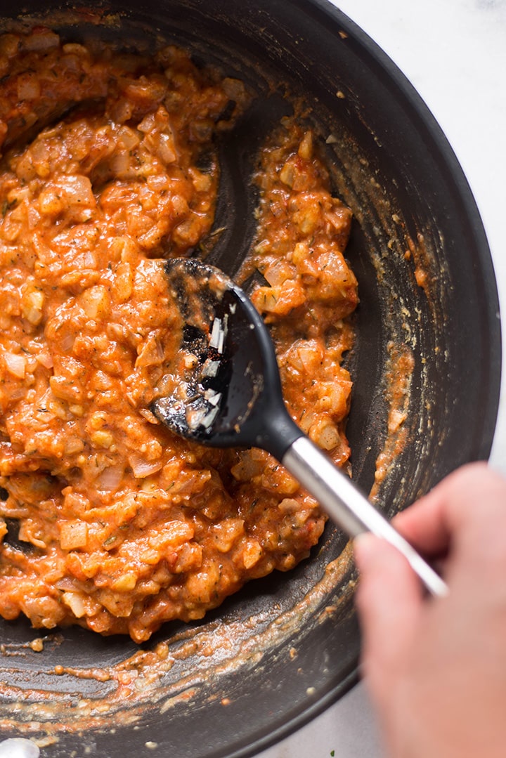 Skillet filled with cooked onion, garlic, and chickpea flour which has the tomato paste and hot sauce added in order to add spice and color to the easy lobster bisque recipe.