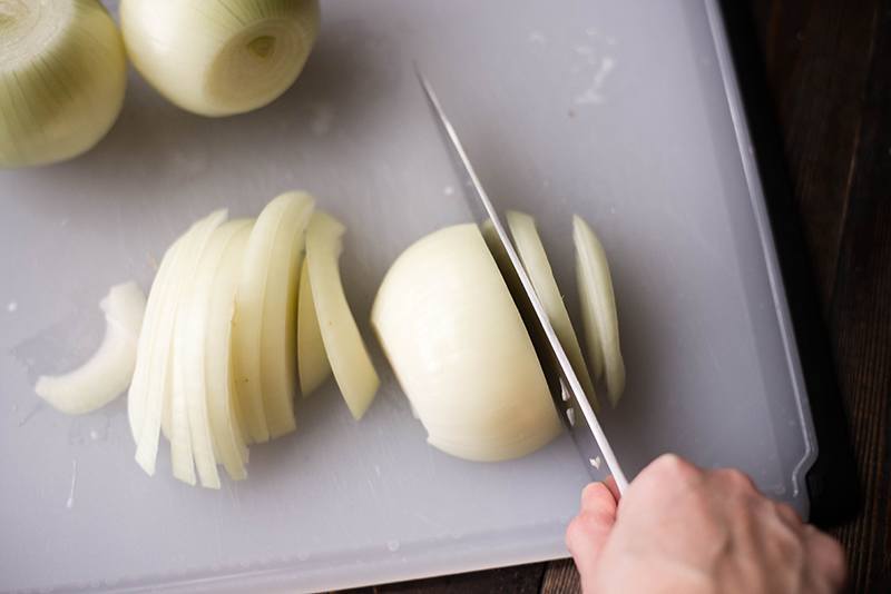 Overhead view of onions being sliced on a cutting board, in preparation for French Onion Soup.