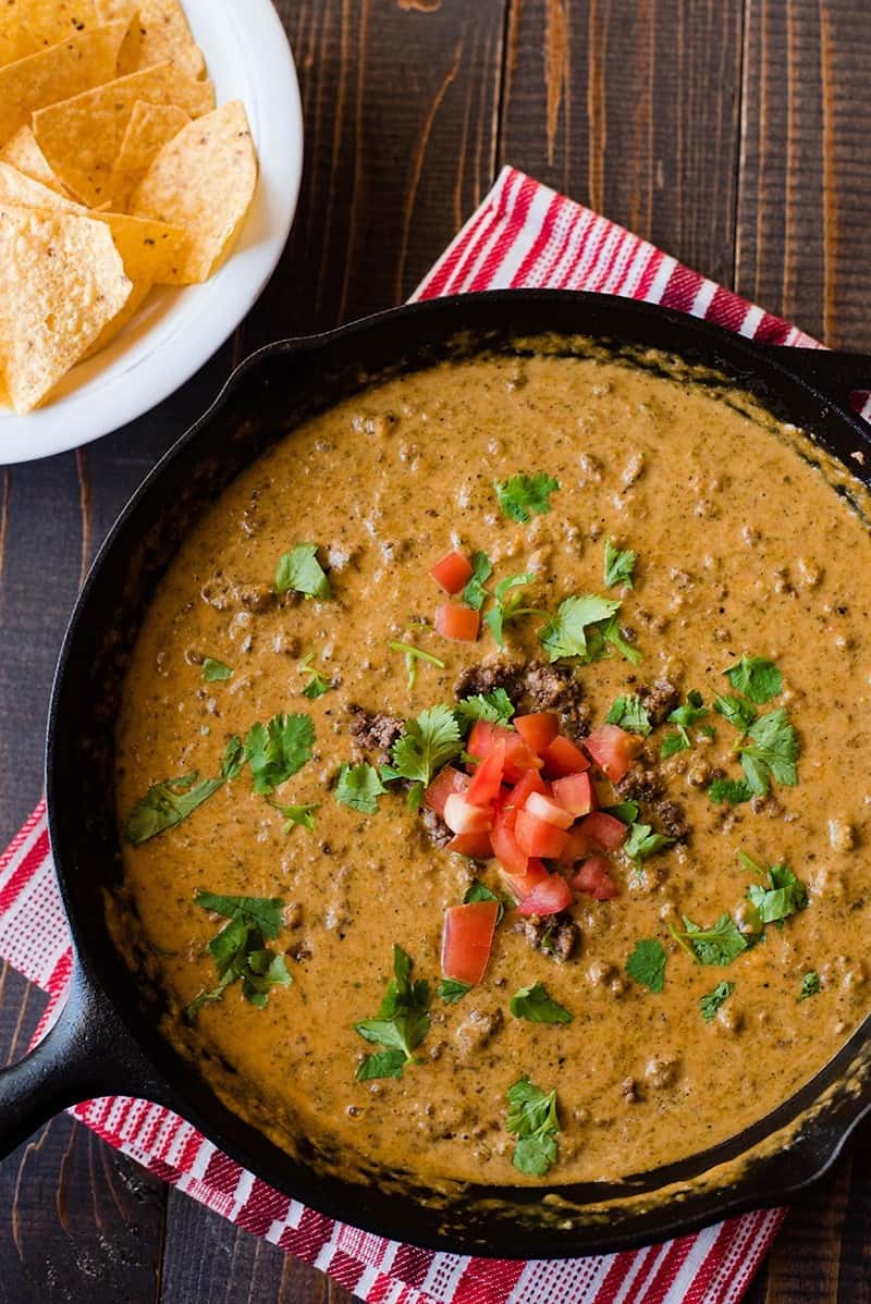 Overhead view of Queso Dip With Ground Beef in a cast iron skillet, topped with cilantro and diced tomatoes.