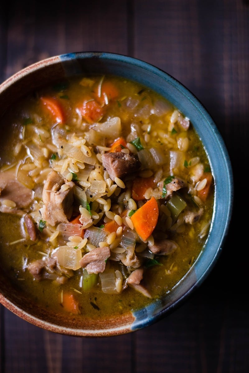 Overhead close-up view of a ceramic bowl containing Lemon Chicken Orzo Soup, including carrots, chicken, and orzo.