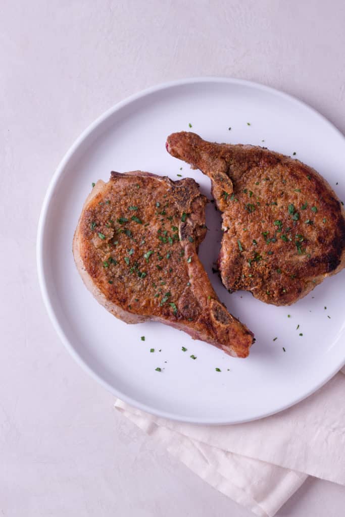 Overhead image of a white plate with two cooked pork chops on it.