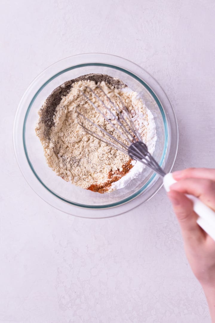 Overhead image of a glass bowl with ingredients including chickpea flour, arrowroot starch, paprika, sea salt, and cayenne pepper being whisked in preparation for Best Juicy Pork Chops.