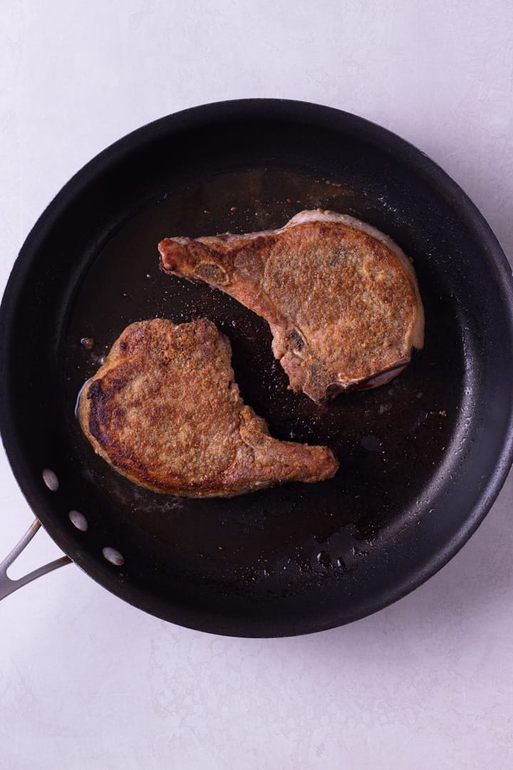 Overhead image of a black skillet containing two cooked Best Juicy Pork Chops.