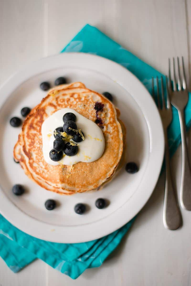 Overhead image of a white plate with a stack of Lemon Blueberry Protein Pancakes, topped with cream and blueberries.