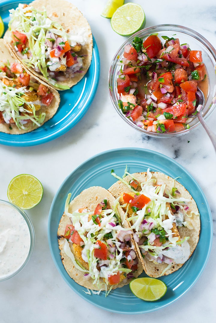 Servings of fresh baja style fish tacos made with corn tortillas and accompanied by bowls of fresh Pico de Gallo sauce and creamy white dill sauce