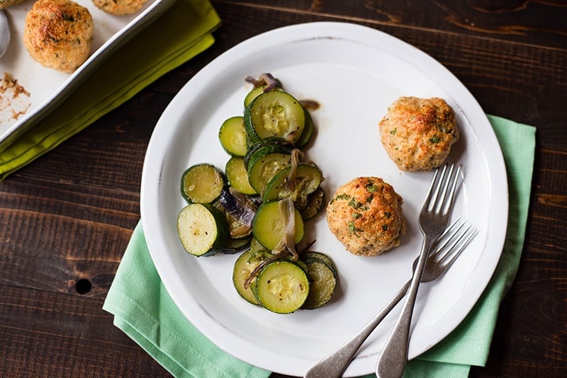 Overhead view of a plate with two baked chicken meatballs alongside the sauteed zucchini for an easy weeknight meal.