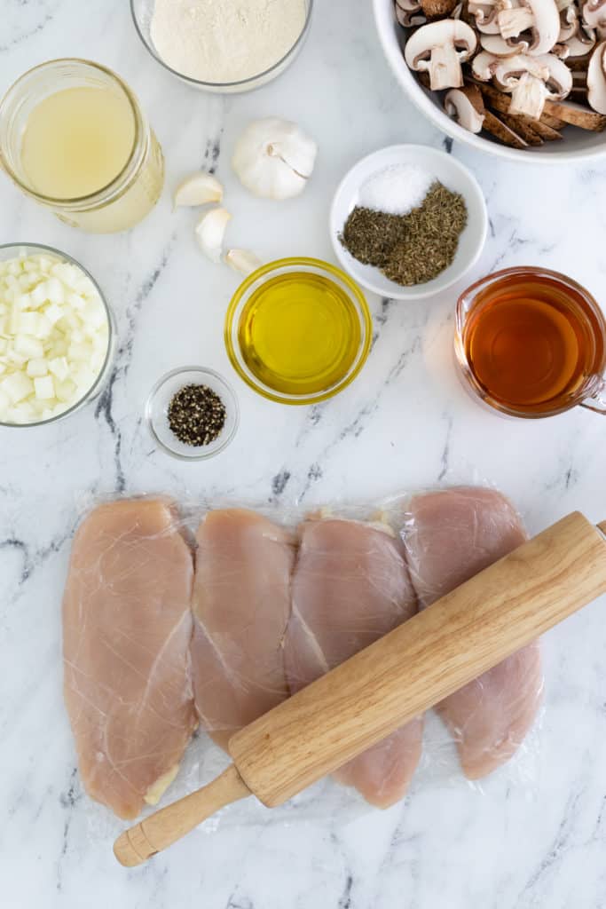 Overhead view of some of the ingredients for the Healthy Chicken Marsala, with the chicken breasts being rolled on the counter to make them thin.