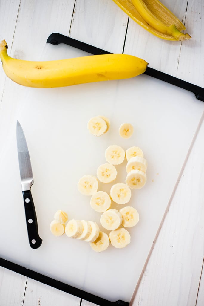Overhead image of a cutting board with sliced bananas, with whole bananas off to the side.