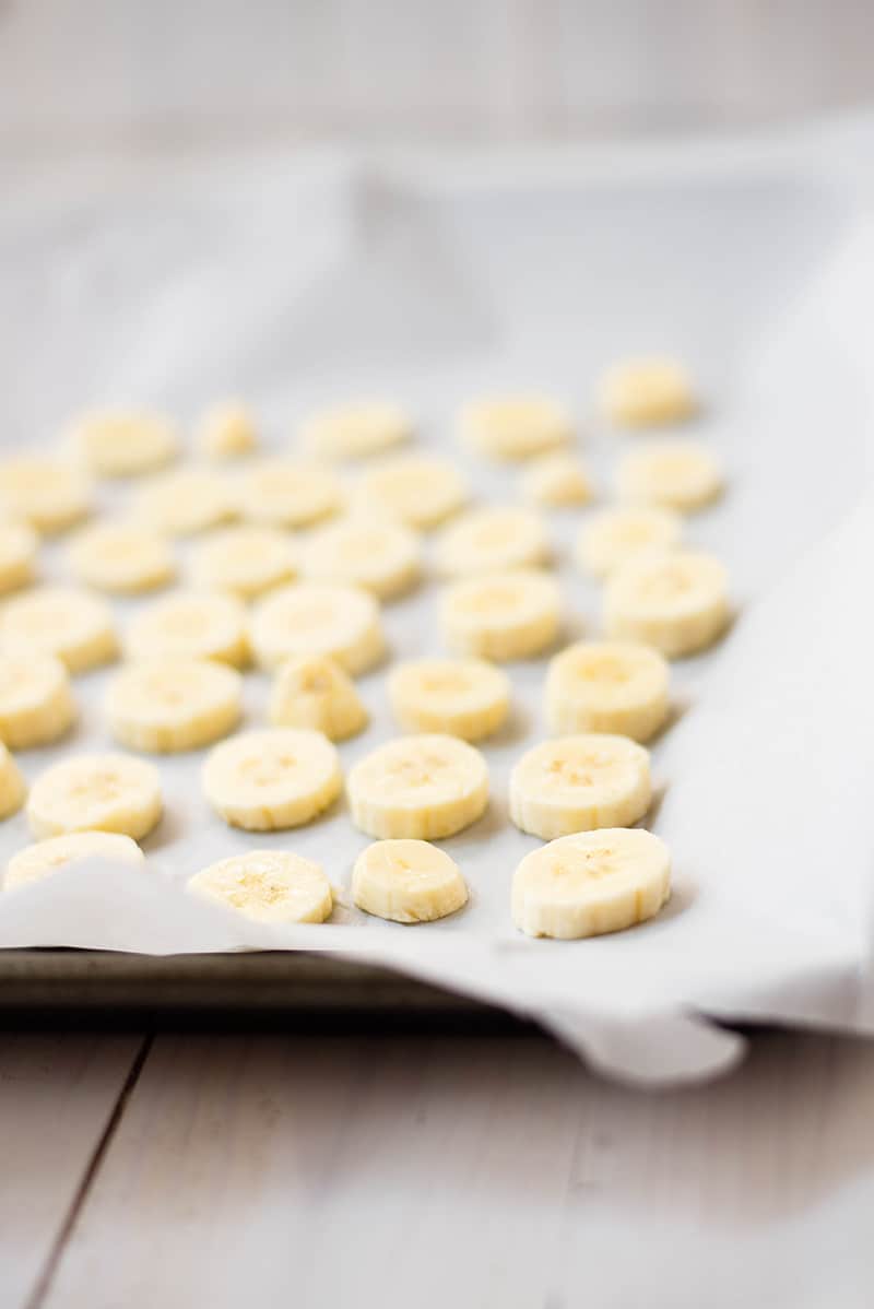 Sliced bananas placed on a lined baking tray, to be frozen and used to make homemade banana ice cream 