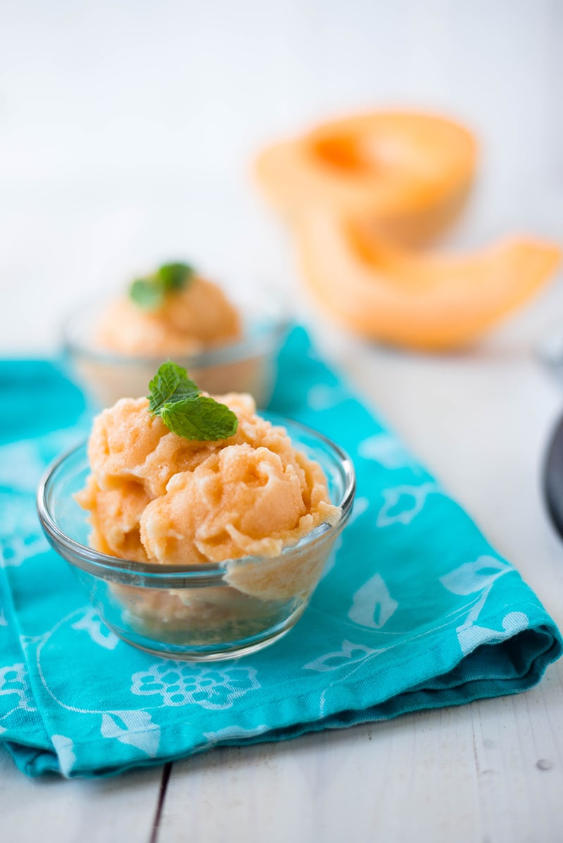 Homemade cantaloupe sorbet served in glass bowls, placed on a turquoise kitchen towel 