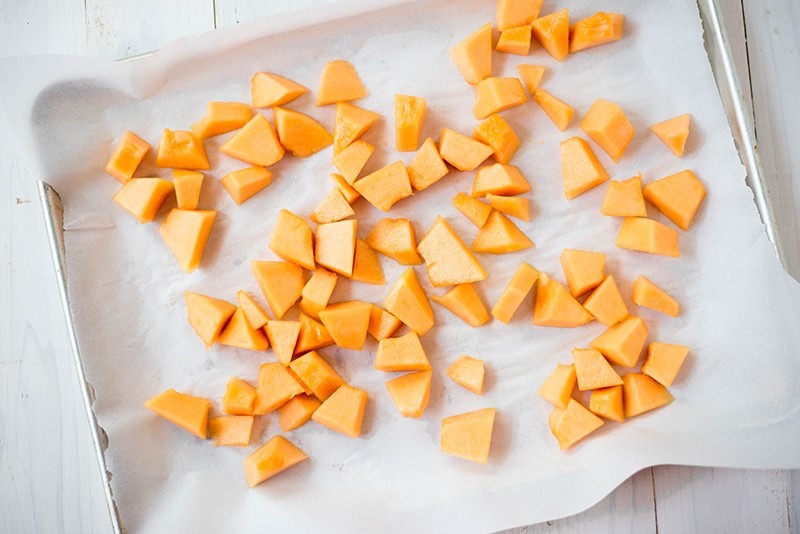 Chopped cantaloupe cubes placed on a baking sheet lined with parchment paper, ready to be frozen to make cantaloupe sorbet 