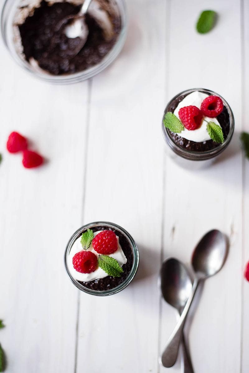 Overhead view of 2 small mason jars of Overnight Chocolate Chia Pudding, garnished with Greek yogurt and raspberries.