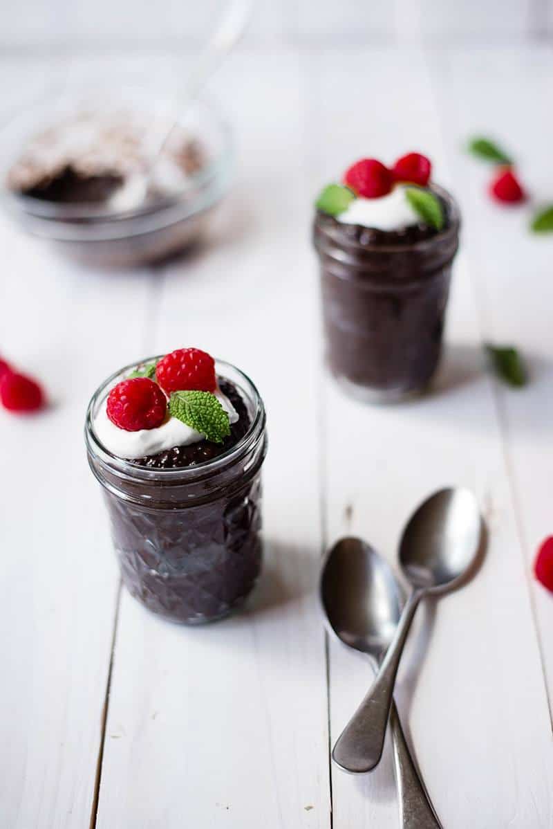Side view of Overnight Chocolate Chia Pudding, served with Greek yogurt and raspberries, in two mason jars.