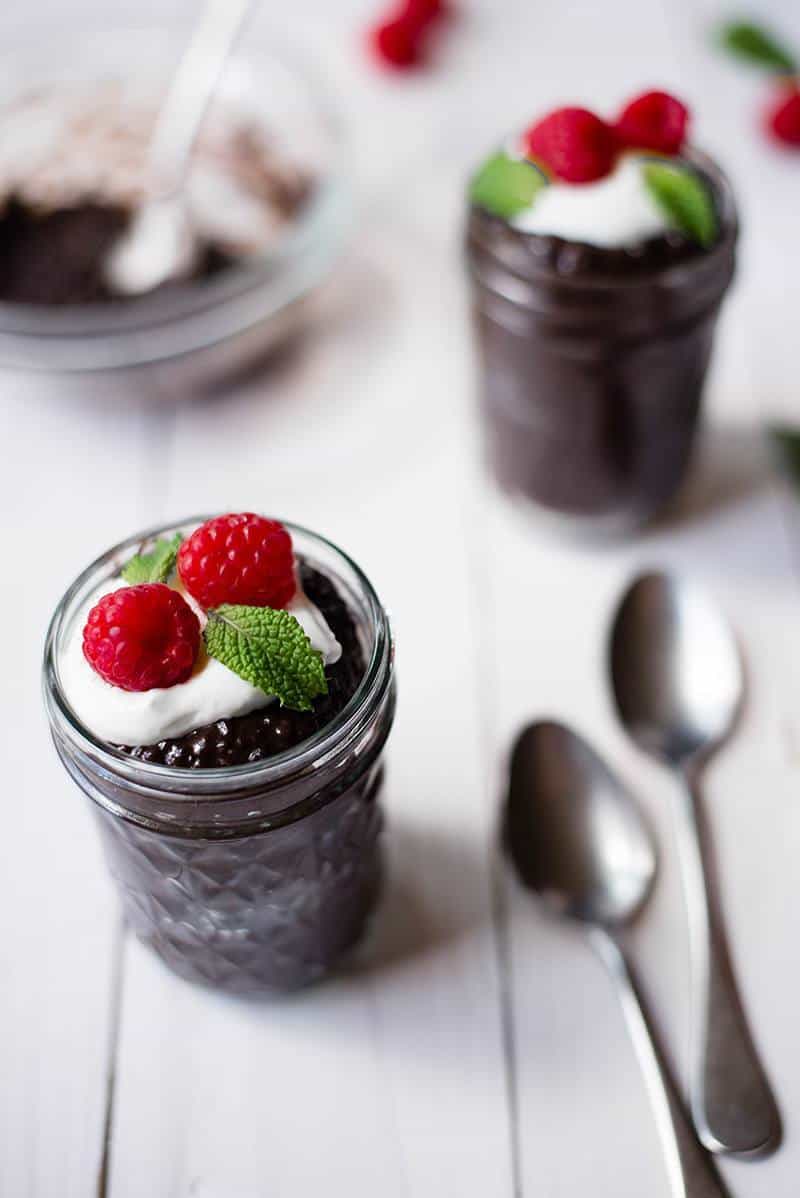 Closeup image of Overnight Chocolate Chia Pudding served in two mason jars, topped with Greek yogurt and raspberries.