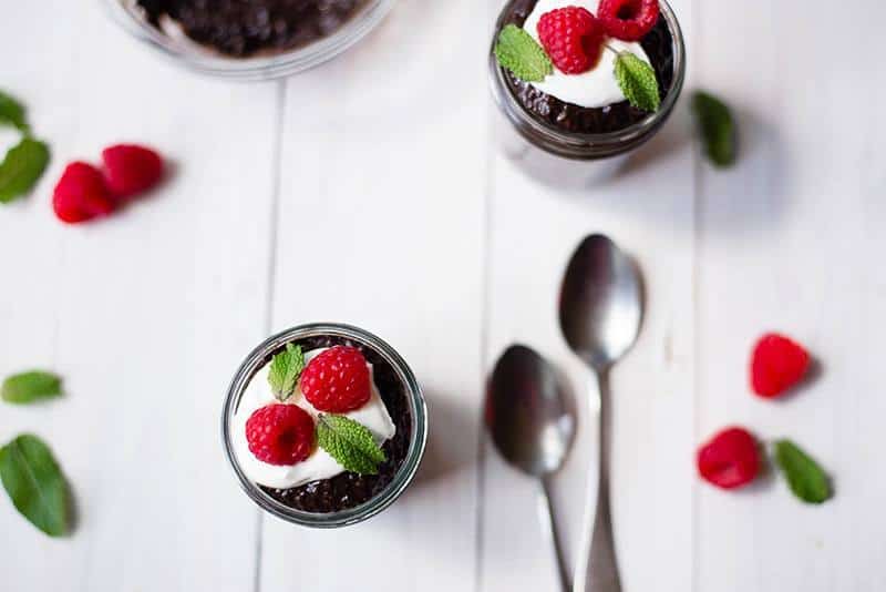 Closeup view of 2 servings of Overnight Chocolate Chia Pudding in mason jars, garnished with Greek yogurt and raspberries.