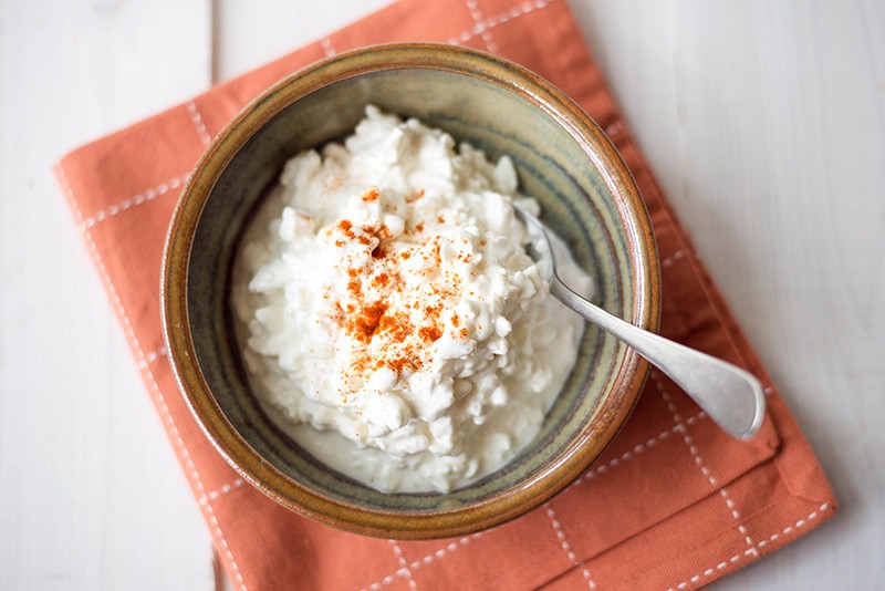 Overhead image of a bowl of full-fat cottage cheese, with a spoon in it and ready to eat.