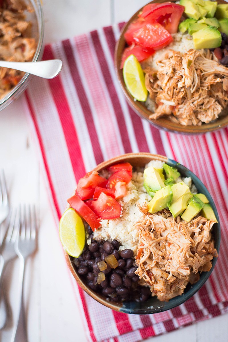Close up photo of slow cooker chicken burrito bowl, loaded with toppings , including avocado, tomato, lime, and black beans.