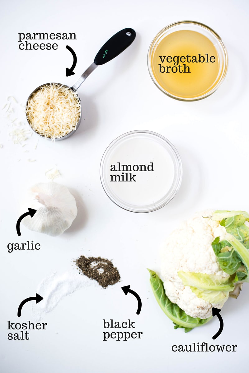 The seven ingredients needed for how to make cauliflower cheese sauce, including parmesan cheese, almond milk, vegetable broth. garlic, salt, pepper, and fresh cauliflower.