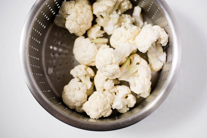Overhead image of a steamer basket which has the fresh cauliflower florets, ready to be steamed to make cauliflower cheese sauce.