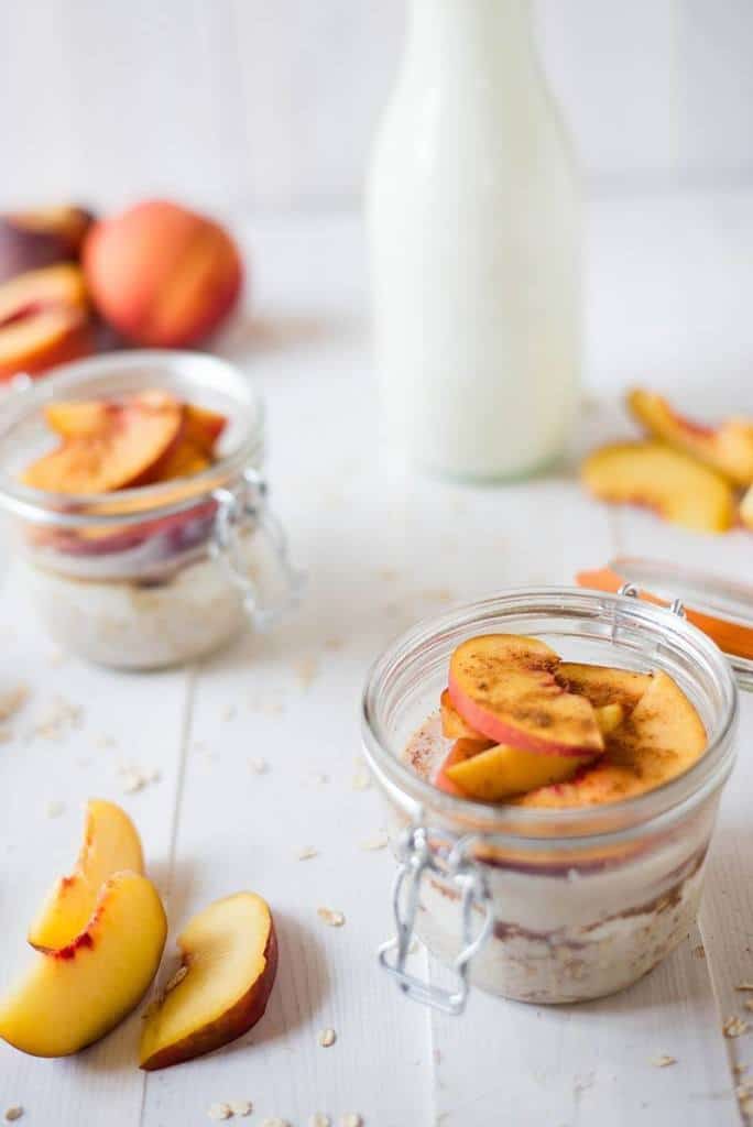 Close up image of glass dishes with overnight oats topped with peaches, with slices of peaches off to the side.