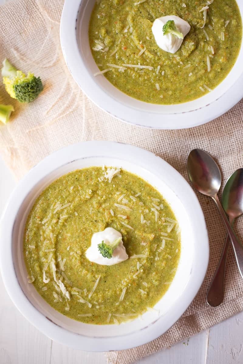 Two bowls of cream of broccoli soup topped with a dollop of plain greek yogurt, ready to eat.