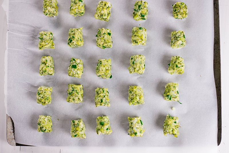 Overhead image of the unbaked lined up broccoli tots that are separated for even baking.
