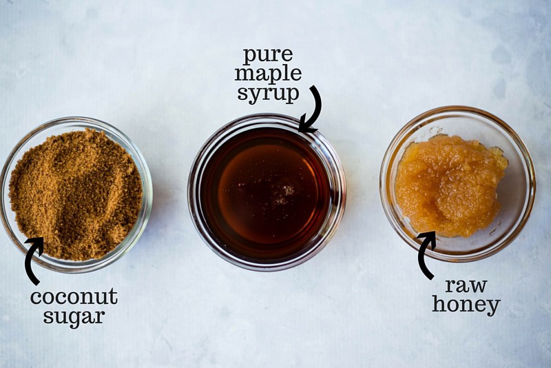 Overhead view of 3 glass bowls, one with coconut sugar, one with pure maple syrup, and one with raw honey.