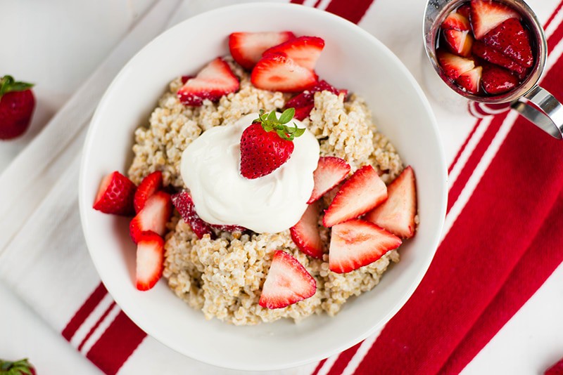 Overhead view of Strawberries And Cream Steel Cut Oats in a white bowl and topped with whipped cream, ideal Healthy Breakfast Idea.