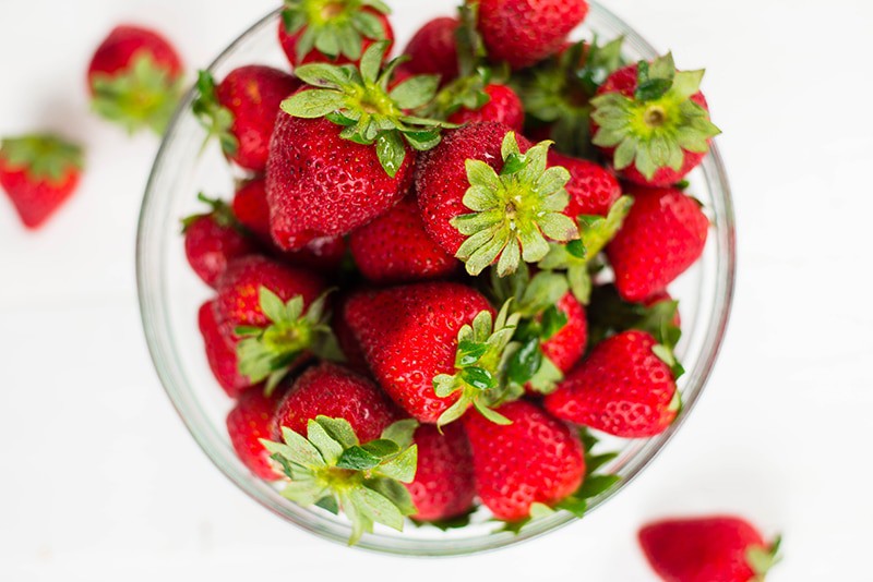 Close up overhead image of a glass bowl filled with strawberries, as a source of Vitamin C.
