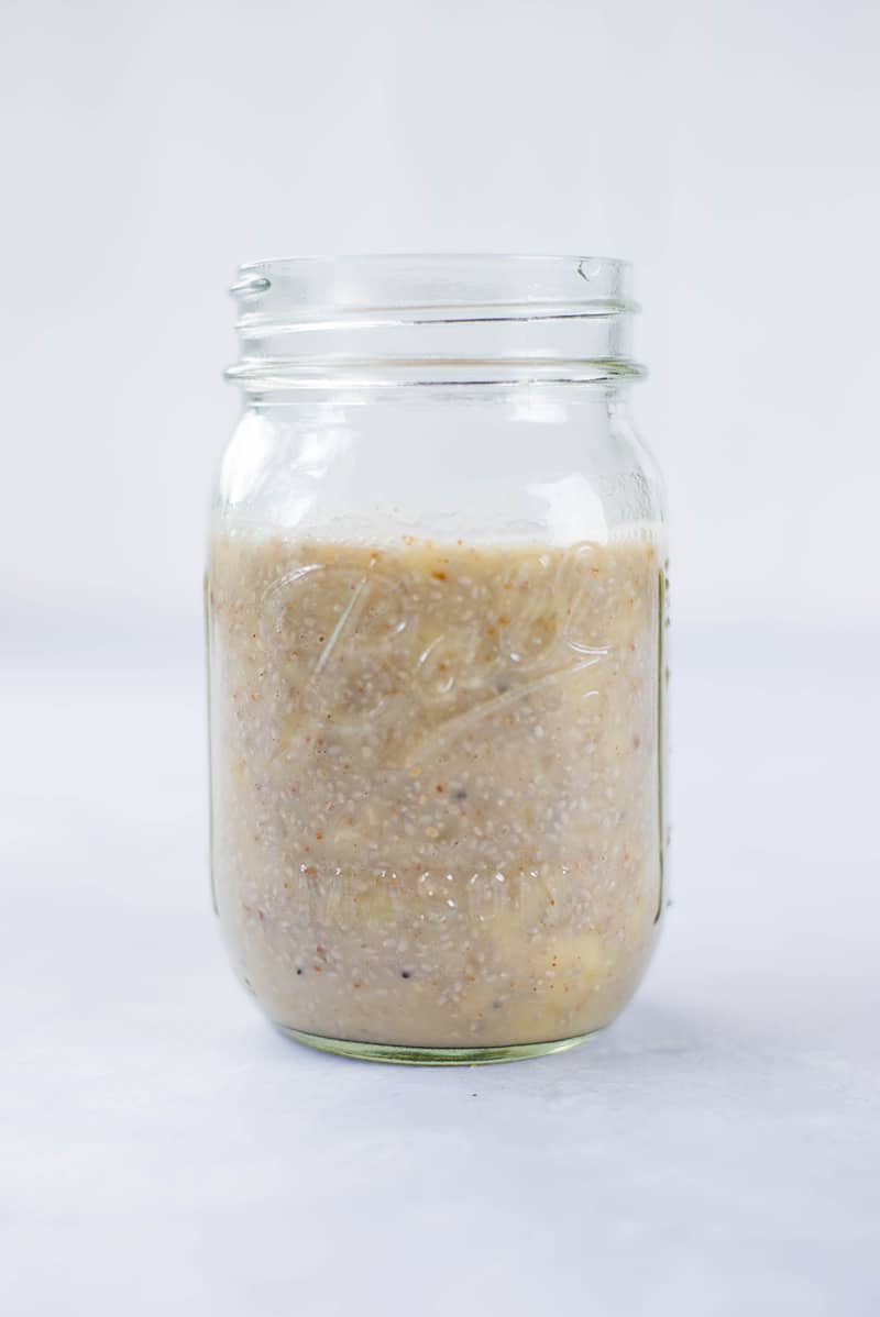 Straight on shot of banana chia pudding before being placed into the fridge, which is in a mason jar against a neutral background 