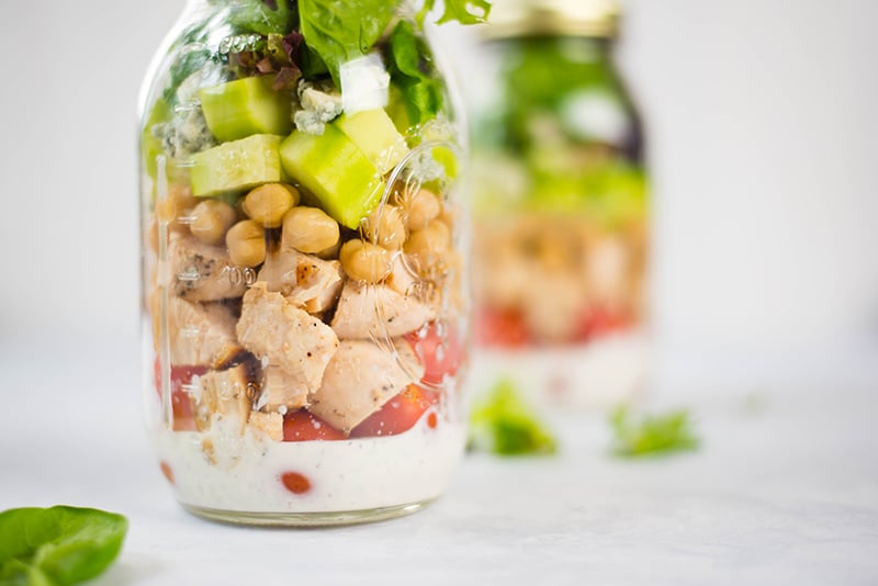 Close up of all the layers of ingredients used to make cobb salad in a jar, placed against a white background 