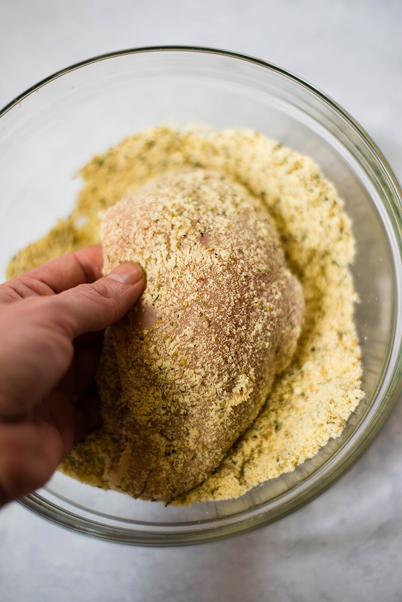 Chicken breast coated in breading mixture, ready to be cooked in a skillet to make the healthy baked chicken Parmesan dish 