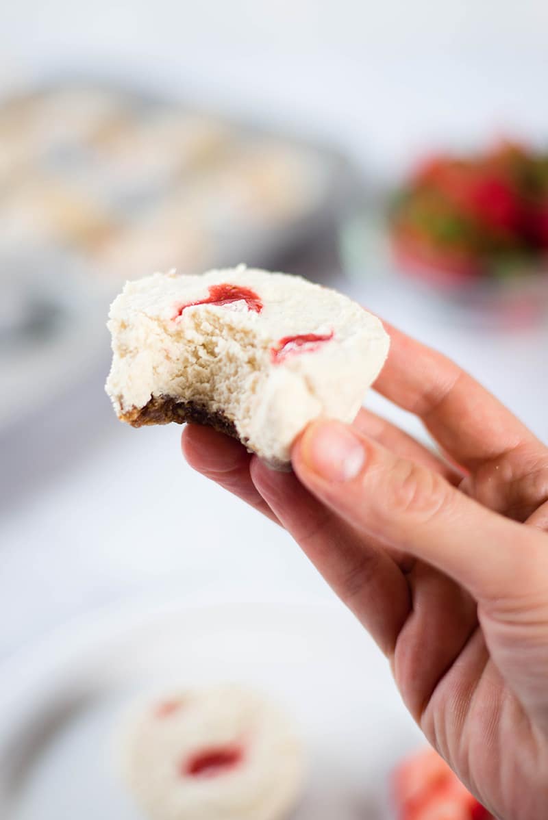 Close up image if a hand holding a mini cheesecake with a bite taken out.