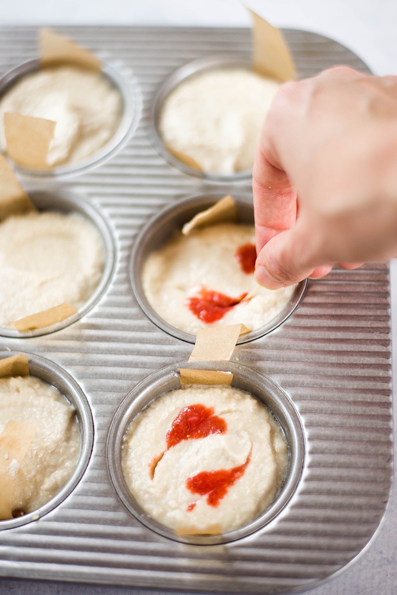 Close up image of the strawberry sauce being swirled into the No Bake Cheesecake Recipe, which has been poured into the muffin tin.