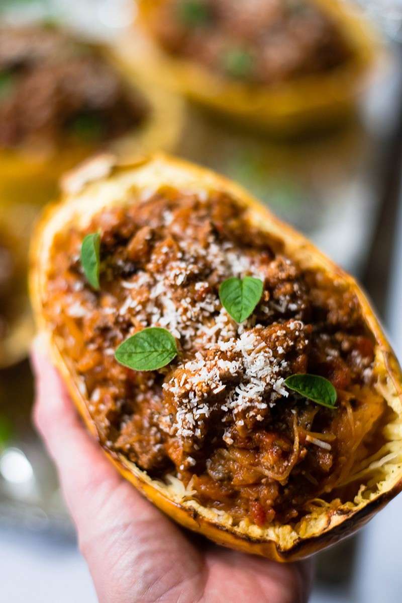 Close up of a stuffed spaghetti squash bowl, garnished with basil leaves and Parmesan cheese