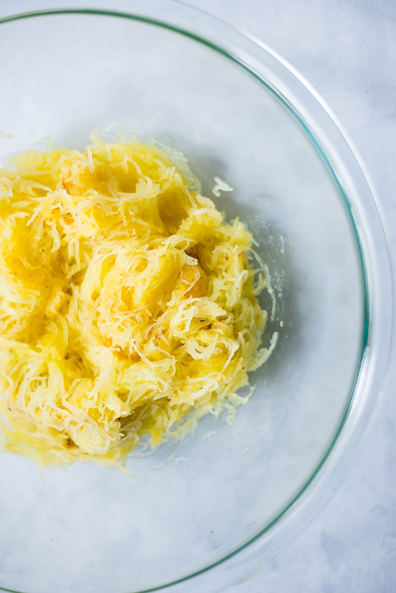 A glass bowl of grated baked squash, ready to be used to stuff spaghetti squash bowls 