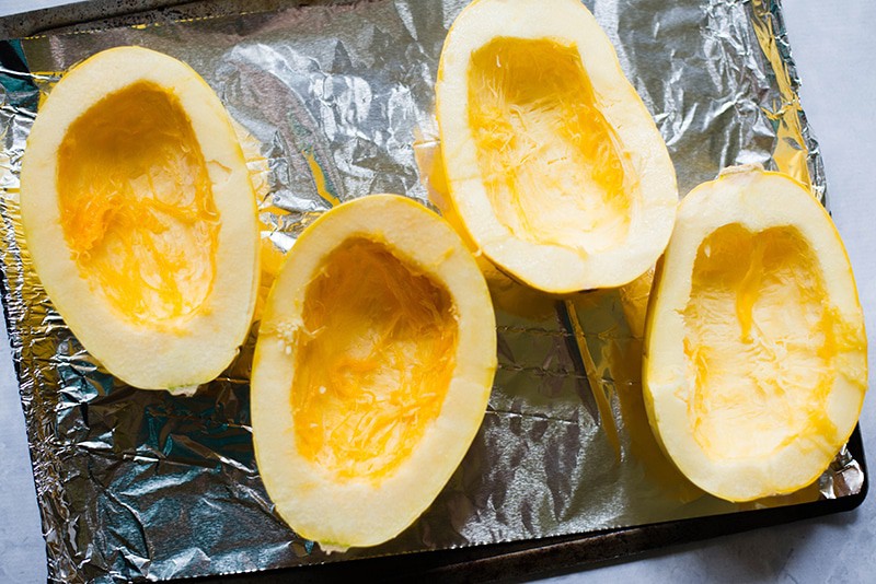 Halved pieces of squash placed on a baking sheet lined in aluminum foil, ready to be baked for spaghetti squash bowls recipe 