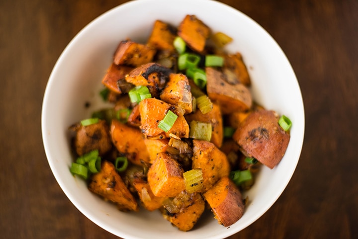 Close up shot of the sweet potato hash recipe in a white bowl, ready to be served and topped with sliced green onions.