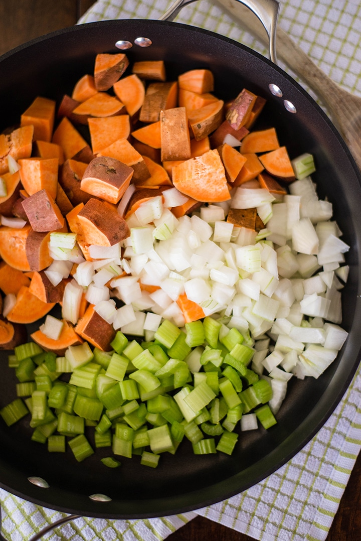 Large skillet filled with uncooked sweet potatoes, white onion, celery, and spices, ready to cook to make the sweet potato hash.