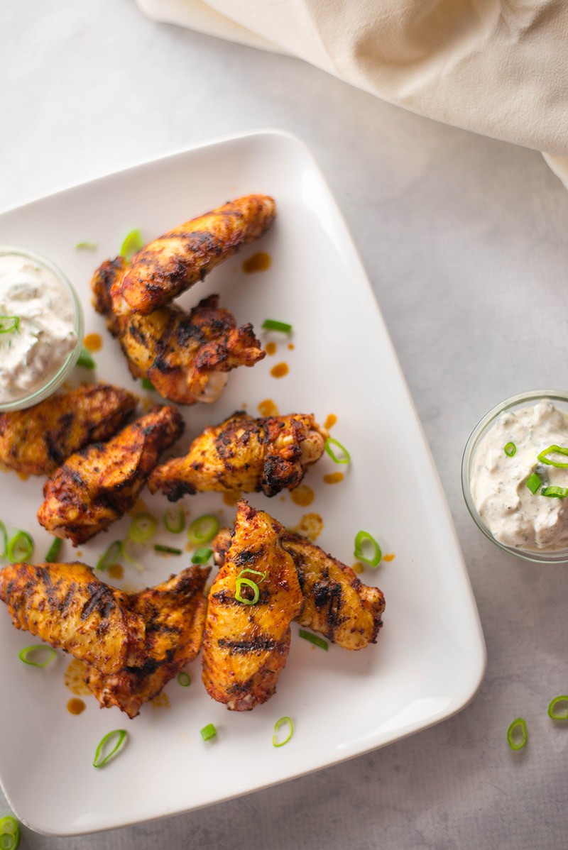 Close up overhead view of Grilled Chicken Wings with Yogurt Ranch Dip, on a white plate with the dip in a bowl beside the wings.