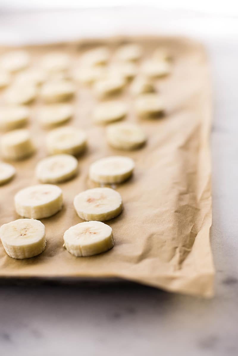 Banana slices placed on a tray lined with parchment paper, ready to be frozen to make chocolate banana ice cream 