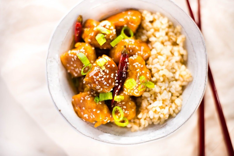 Overhead image of a bowl of Healthy General Tso's Chicken, topped with green onions and sesame seeds.