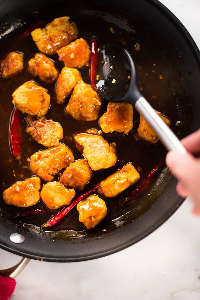Overhead view of a skillet, with a spoon stirring Healthy General Tso's Chicken.
