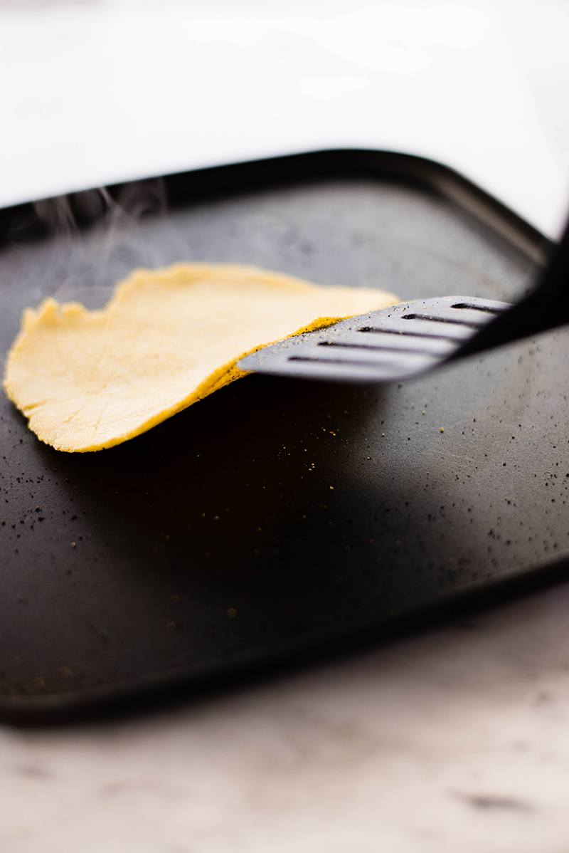 Flipping a homemade corn tortilla over on the hot skillet.