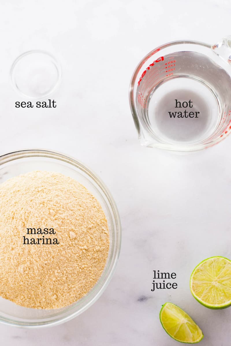Four ingredients required for homemade corn tortillas, including masa harina, sea salt, lime juice, and hot water, ready to be mixed together.