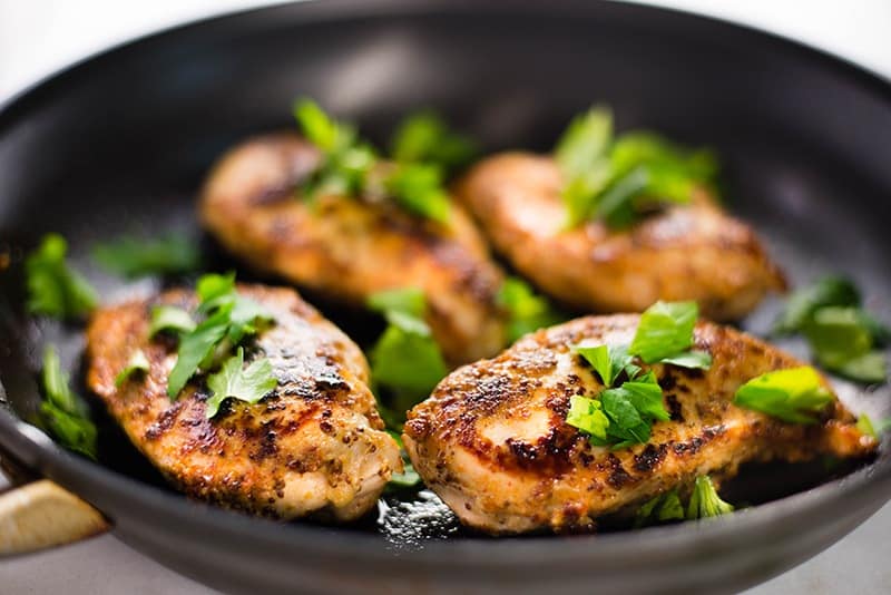 Honey mustard chicken cooked in a skillet and garnished with chopped Italian parsley 